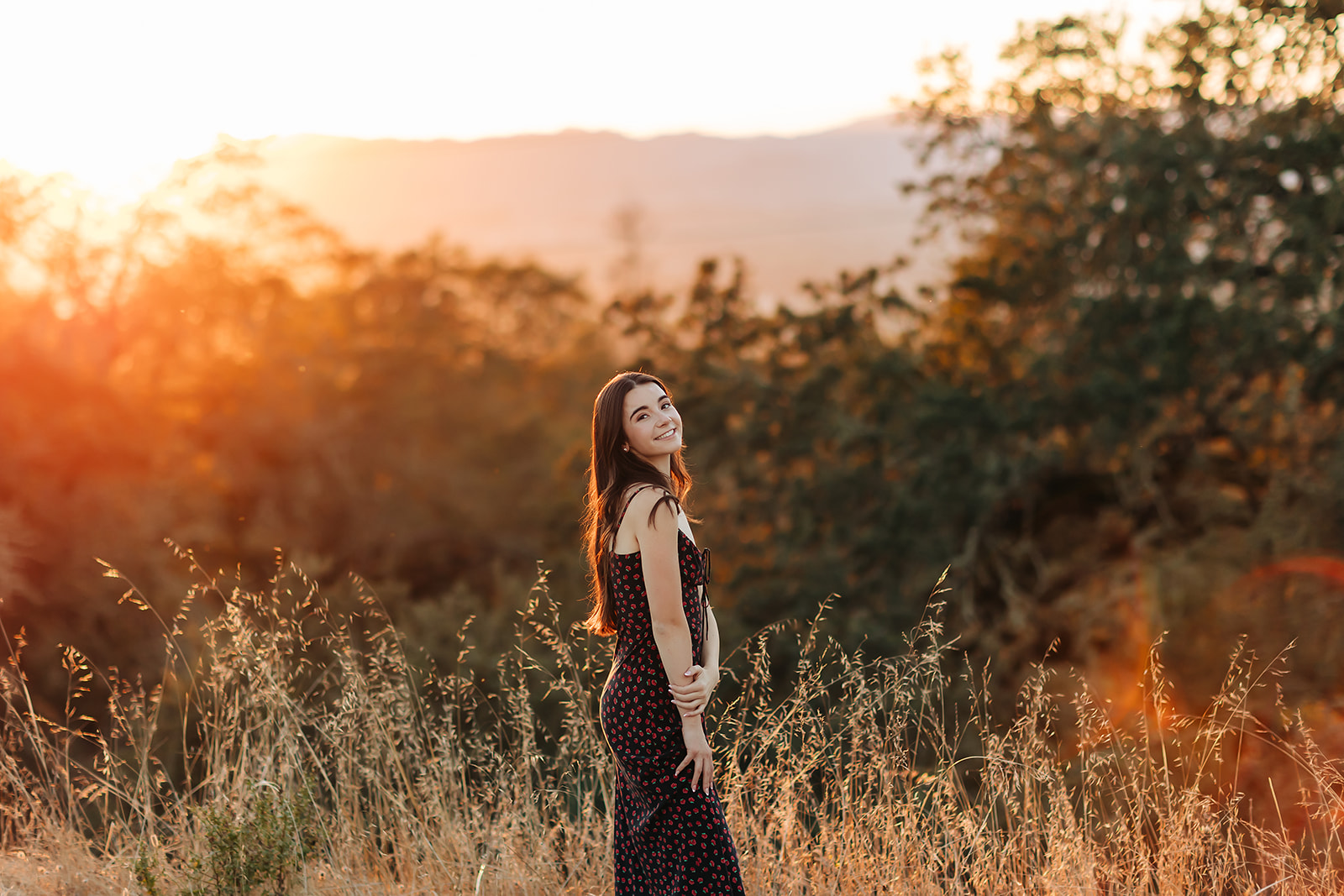 A gorgeous senior girl standing and posing in front of a field during sunset