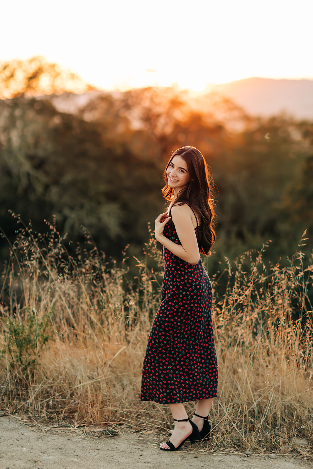 a girl standing in a field during sunset posing