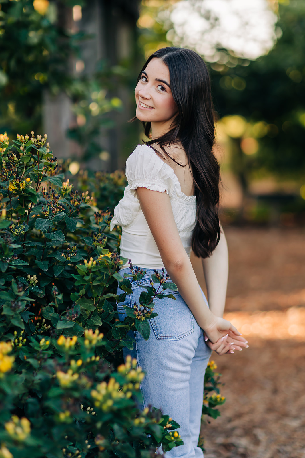 a girl standing next to some bushes posing